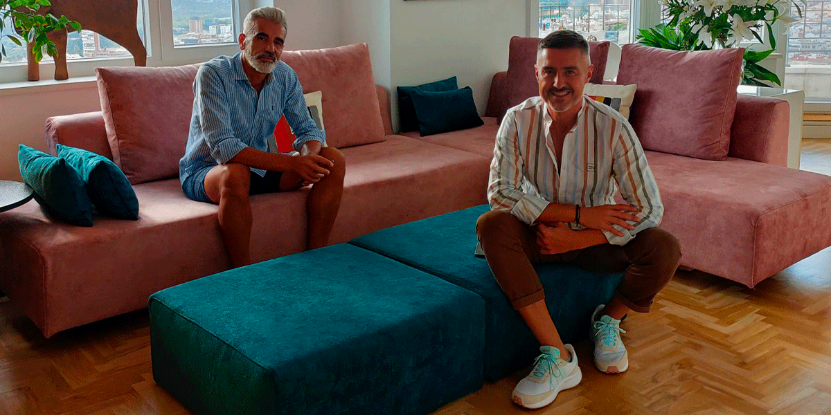 Pepe y Paco, en su salón con sofás rosa y pufs azul petróleo.