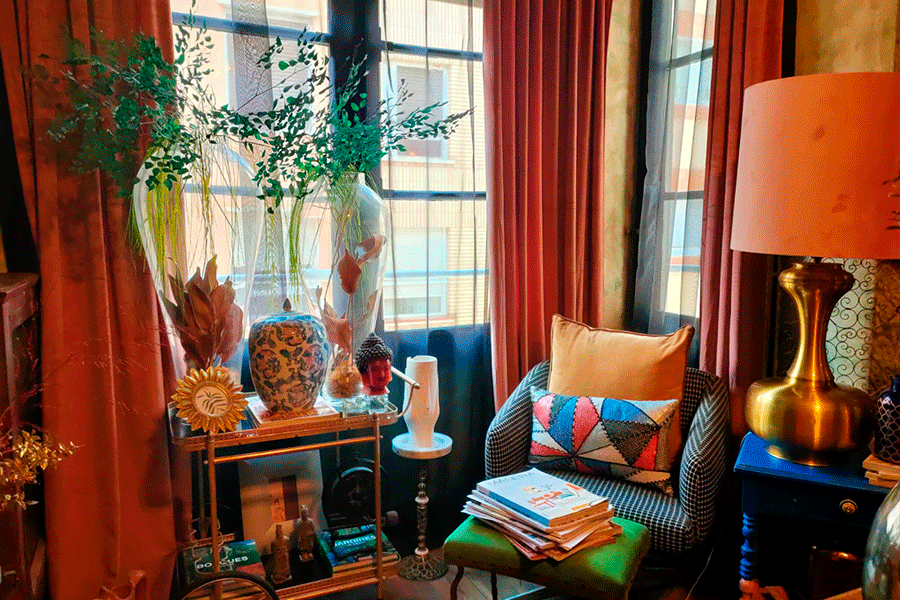 Rincón de lectura: cortinas de terciopelo, lámpara dorada y sillón tapizado con libros al pie.
